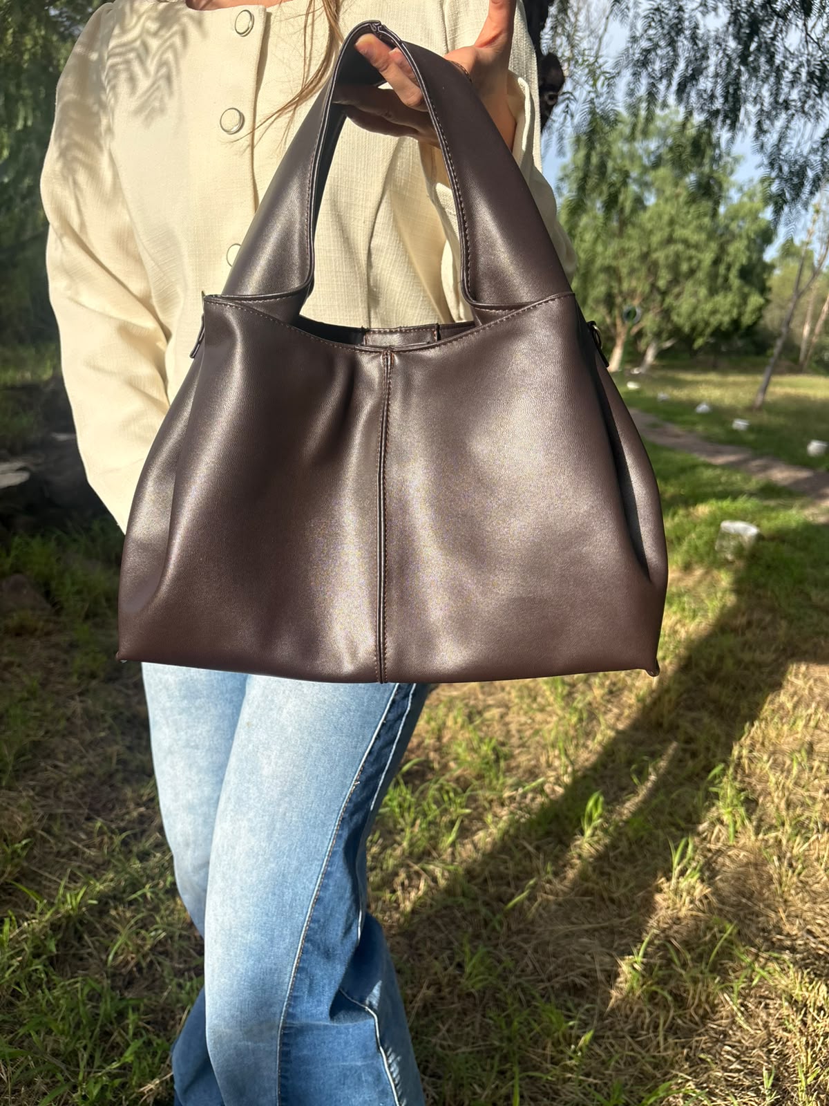 Bolso tote CERDEÑA en piel chocolate, sostenido en la mano por una modelo en exterior