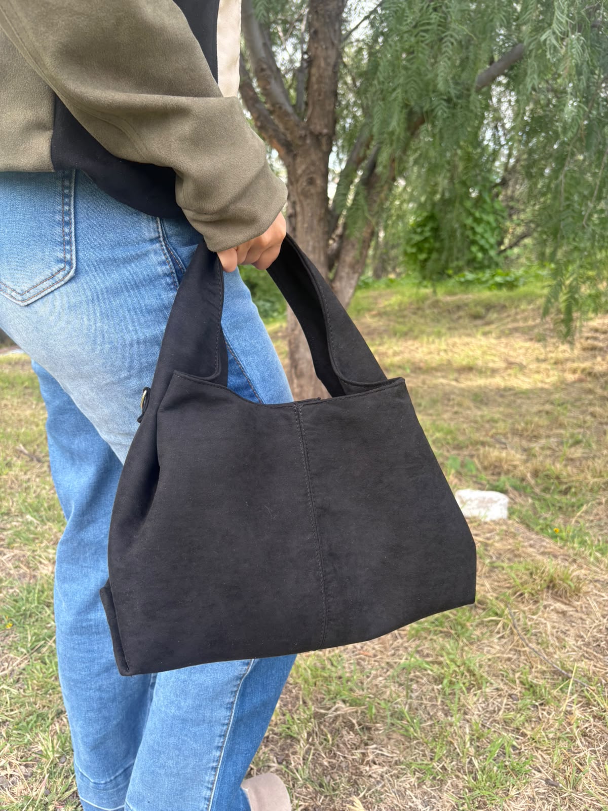 Bolso tote CERDEÑA en gamuza negra, sostenido en la mano por una modelo en exterior