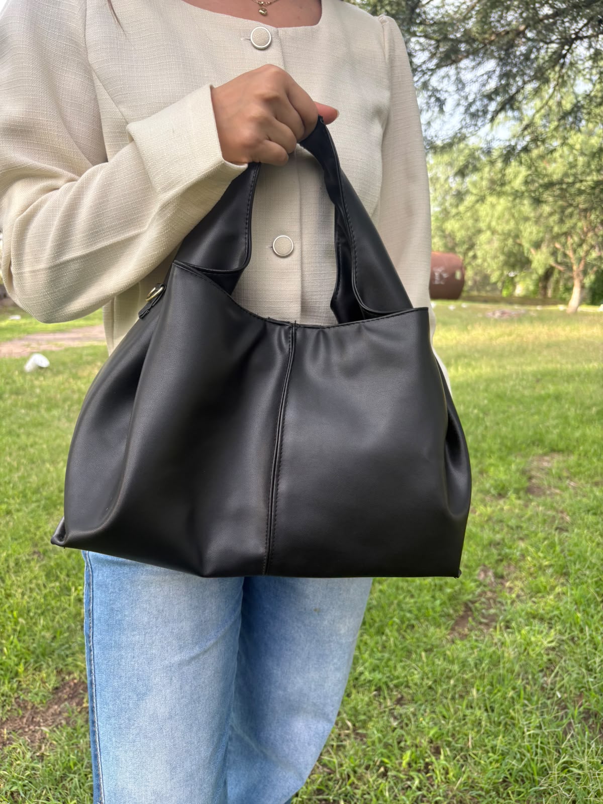 Bolso tote CERDEÑA en piel negra, sostenido en la mano por una modelo en exterior
