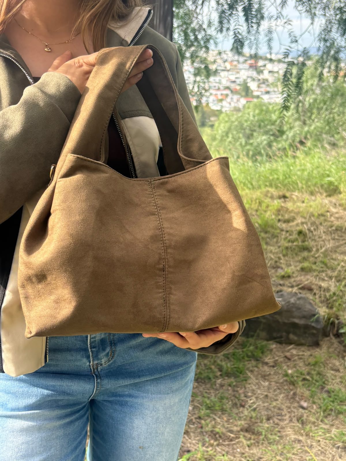 Bolso tote CERDEÑA en gamuza, sostenido en la mano por una modelo en exterior
