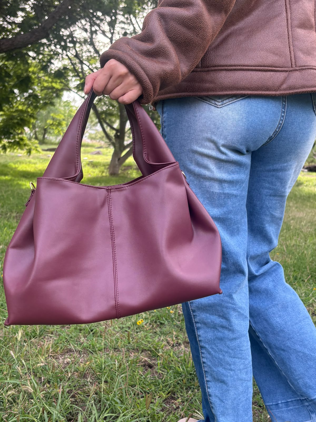 Bolso tote CERDEÑA en piel vino, sostenido en la mano por una modelo en exterior