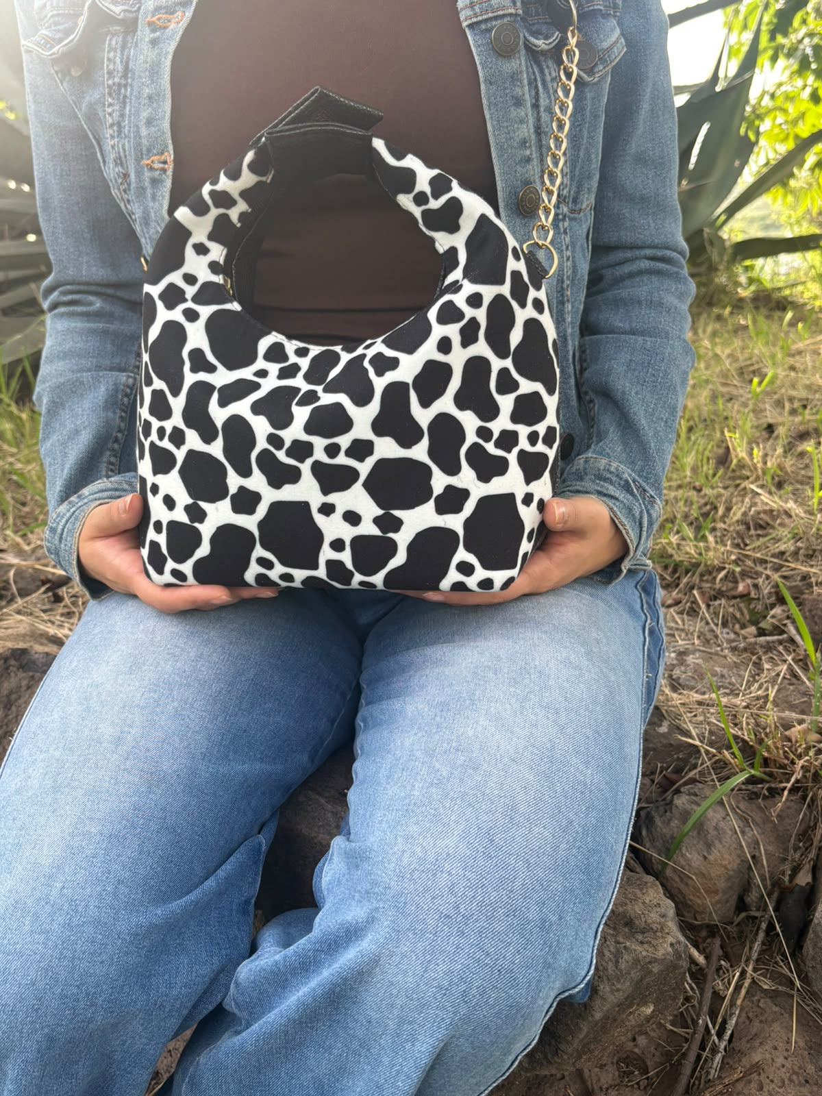 Bolso LUCCA con estampado de vaca en blanco y negro, sostenido sobre el regazo por una modelo sentada