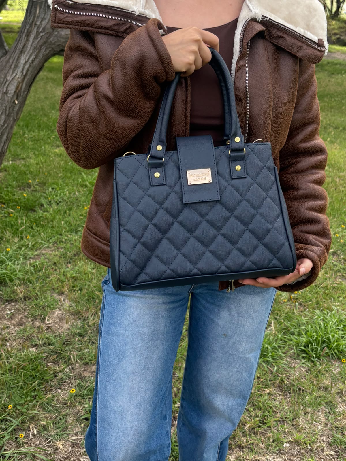 Bolso PALERMO capitonado en azul marino, sostenido en la mano por una modelo en exterior