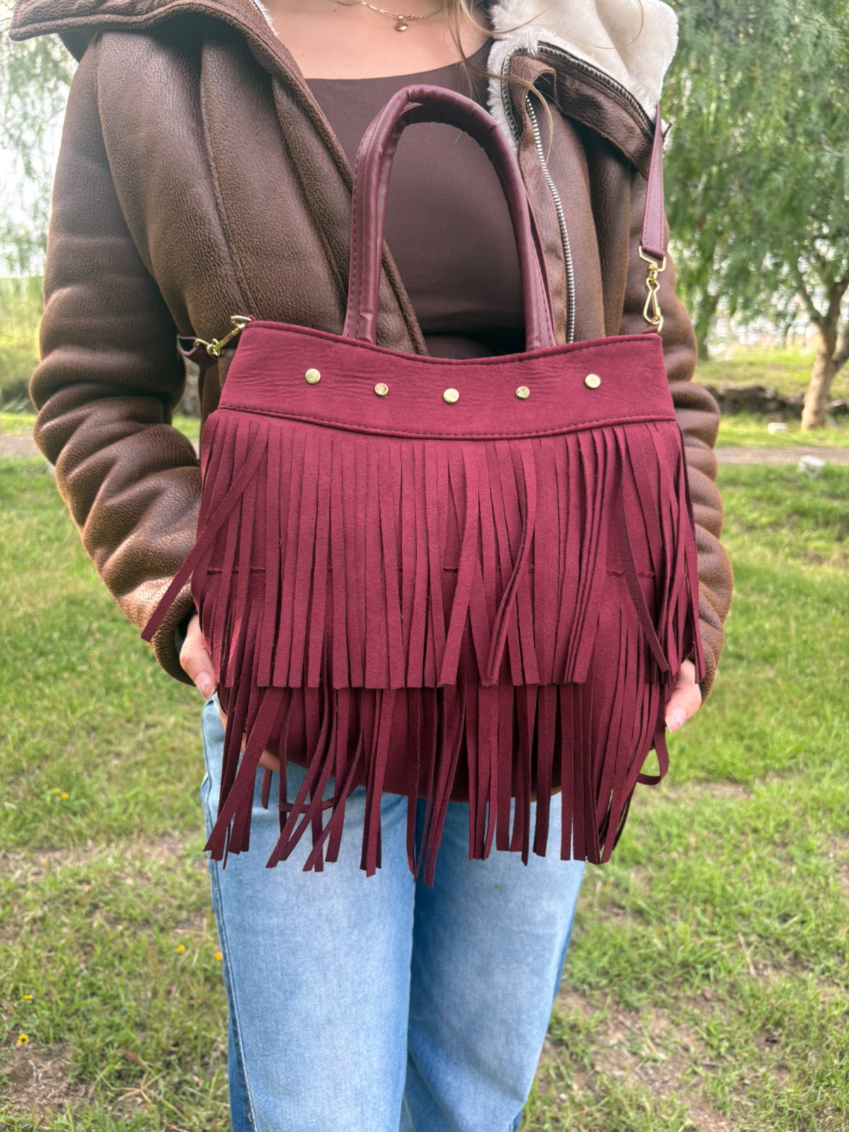 Bolso RAVENA de flecos en gamuza vino, sostenido en la mano por una modelo en exterior