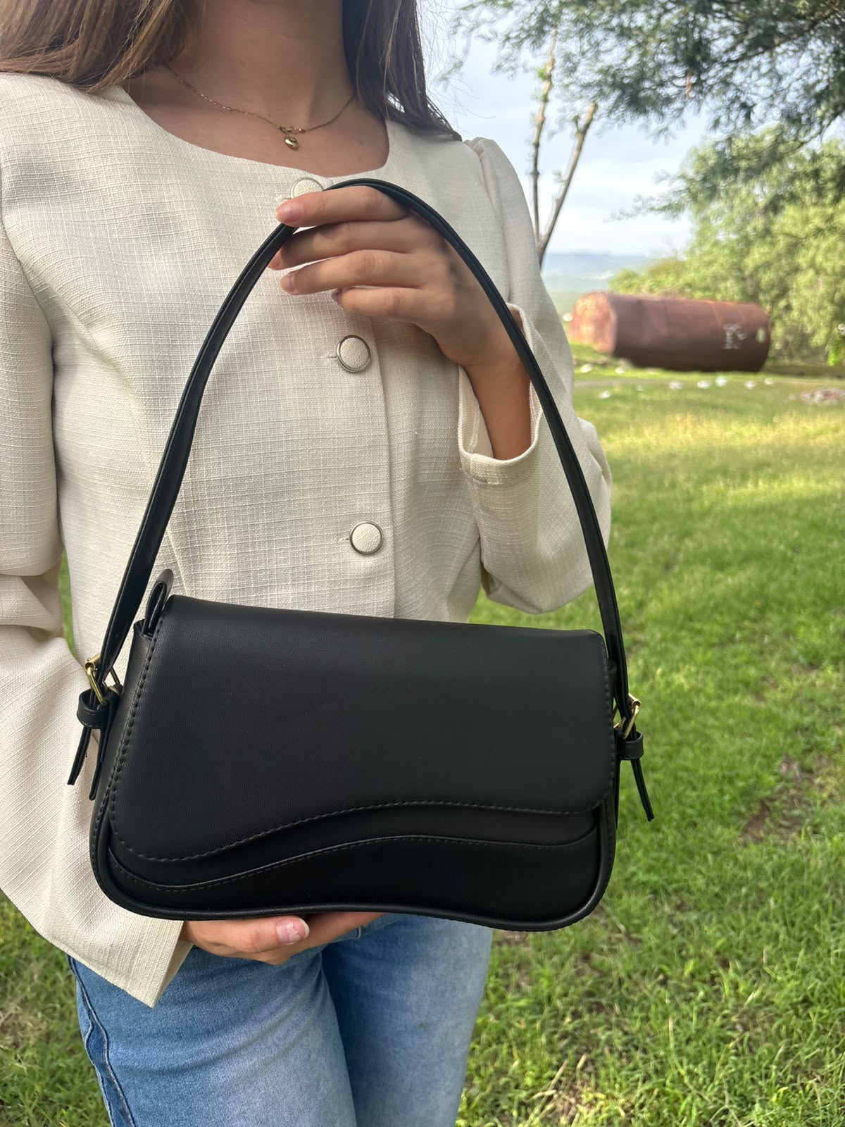 Bolso baguette SAVONA negro con solapa curva, colgado de la mano de una modelo en exterior